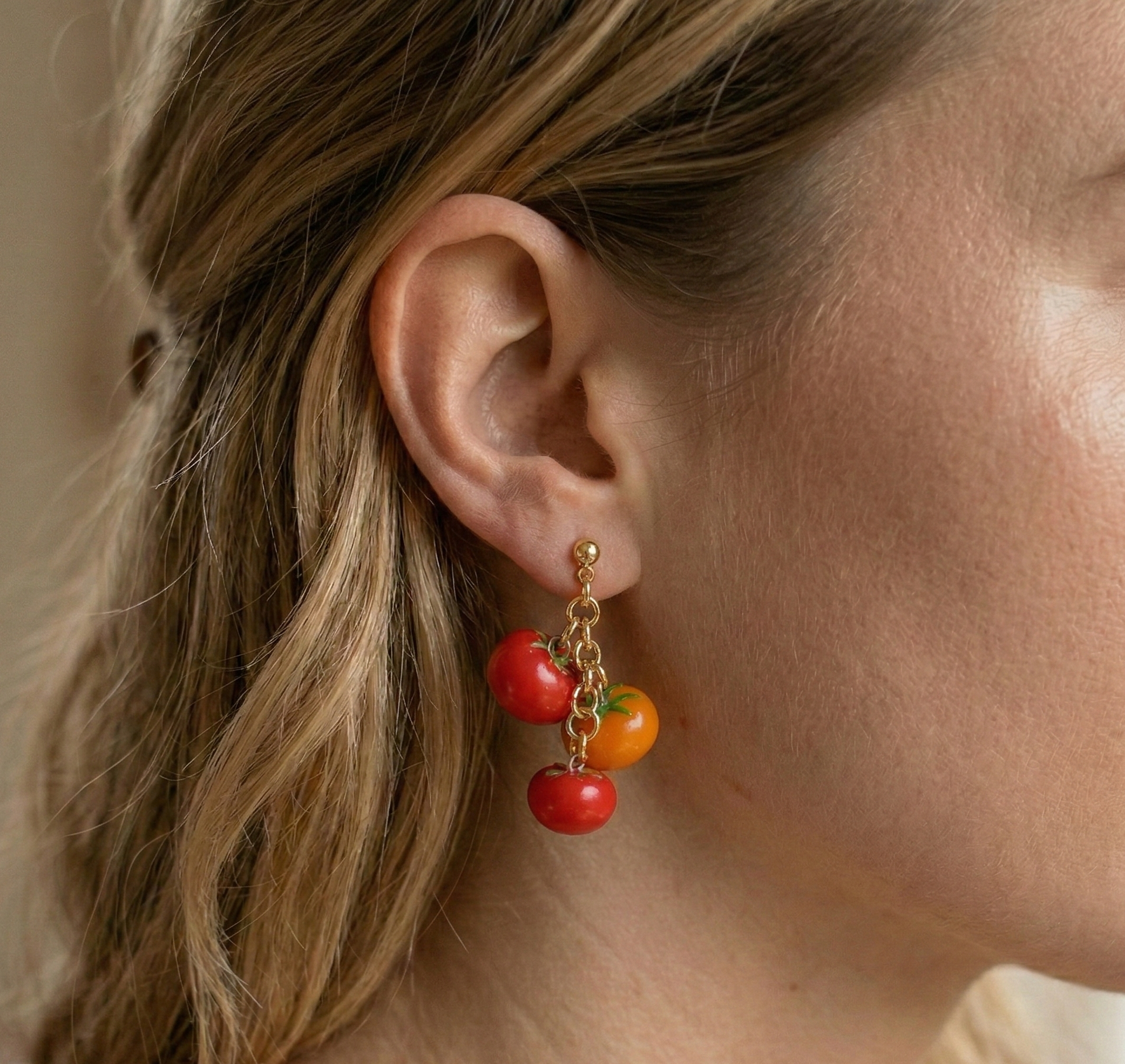 Cherry tomato dangle earrings in red and orange polymer clay, worn on a model's ear - handmade statement jewellery by Clay by KM